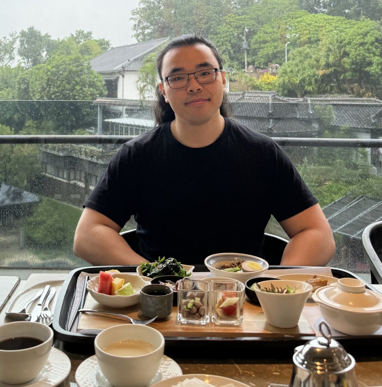 Braden Koh at a table by a rain-streaked window, part-way through breakfast.